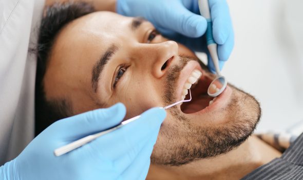 smiling-young-man-sitting-dentist-chair-while-doctor-examining-his-teeth (1)